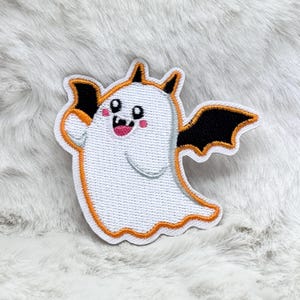 Peut inclure: Écusson en forme de fantôme blanc avec une bordure orange, des ailes de chauve-souris noires et un visage souriant. Le patch a un design mignon et cartoon, parfait pour Halloween ou les créations sur le thème de l'épouvante.