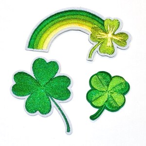 Peut inclure: Écussons brodés sur le thème de la Saint-Patrick. Comprend un arc-en-ciel vert et jaune, un trèfle à quatre feuilles et deux autres trèfles verts. Chaque écusson a une bordure blanche et est posé sur un fond blanc.