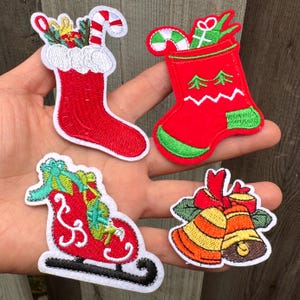 May include: Four Christmas-themed embroidered patches. Includes a red stocking with a candy cane, a red sleigh with gifts, a pair of bells, and a red stocking with green accents and a candy cane.