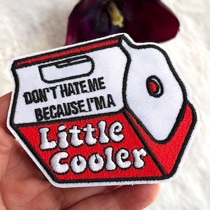 May include: Embroidered patch in the shape of a cooler, with a white top and red bottom. The patch reads "DON'T HATE ME BECAUSE I'M A Little Cooler" in black text. A black border outlines the patch.