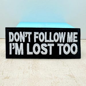 Może przedstawiać: Czarna haftowana naszywka z białym tekstem, który brzmi "Nie idź za mną, ja też jestem zagubiony".
