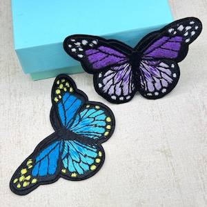 May include: Two embroidered butterfly patches. One butterfly is purple and the other is blue.