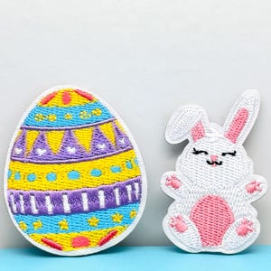 Puede incluir: Parches bordados con temática de Pascua. Un parche es un huevo con un diseño colorido de amarillo, azul, morado y rojo. El otro parche es un conejito blanco con detalles en rosa. Ideales para añadir a ropa o accesorios.