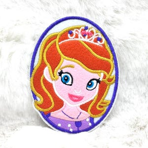 May include: Embroidered patch of a cartoon princess with red hair, blue eyes, and a tiara. The oval-shaped patch has a purple border and a white background. The princess is wearing a purple dress.