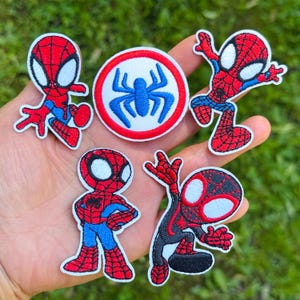 May include: A set of five embroidered patches featuring four cartoon-style figures in red and blue spider-themed suits with large white eyes, and one circular patch with a blue spider emblem centered on a white background with a red border.