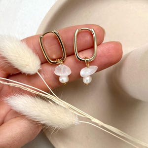 Könnte beinhalten: Goldene Creolen mit einem weißen Stein und einem Perlenanhänger, der an jeder Creole hängt.