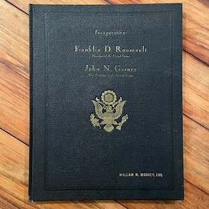 May include: A black hardcover book with gold embossed text reading Inauguration, Franklin D. Roosevelt, President of the United States, John N. Garner, Vice President of the United States, and William M. Mooney, Esq., featuring a central eagle emblem.
