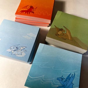 May include: Four stacks of colorful sticky notes with dragon illustrations. The top note of each stack features a different dragon: red, green, light blue, and blue. The background of each note is a gradient color that matches the dragon.
