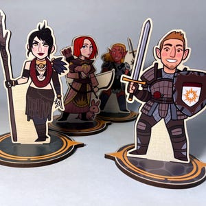 May include: Wooden character cutouts of fantasy figures. One figure holds a staff, another a bow and arrow, a third a sword, and the last a sword and shield. Each character stands on a circular base with a decorative border.