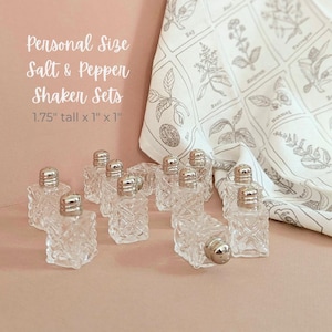 May include: Clear glass salt and pepper shakers with silver lids. The shakers are 1.75 inches tall and 1 inch wide. A white and gray botanical print cloth is in the background. Text on the image reads "Personal Size Salt & Pepper Shaker Sets."
