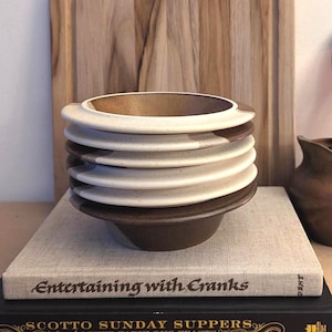 May include: A stack of five ceramic bowls with a two-tone design. Each bowl features a speckled cream-colored rim and a solid dark brown base. The bowls are arranged vertically, creating a layered appearance with alternating cream and brown sections.