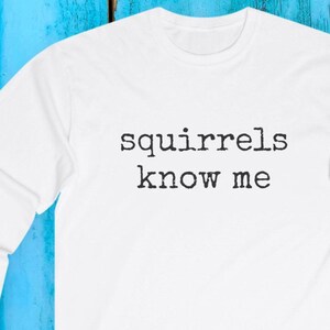 Puede incluir: Sudadera blanca de cuello redondo con la frase "squirrels know me" impresa en negro. La frase está centrada en el pecho. La sudadera está hecha de un material suave, adecuada para uso casual.