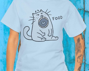 May include: A light blue t-shirt featuring a black line-art illustration of a cat with its mouth wide open, showing teeth and a tongue. The word FOOD is printed in black capital letters next to the cat. The cat has a curved tail and whiskers.