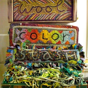May include: A stack of three decorative boxes with the words "wool", "color", and "stash" embroidered on them. The boxes are filled with colorful yarn and fabric scraps. The bottom box is a green suitcase.