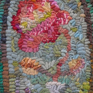 Op de afbeelding: Close-up van een kleurrijk, handgeweven tapijt met een bloemenmotief. Het tapijt is gemaakt van verschillende tinten blauw, groen, roze en rood garen. De textuur van het tapijt is zichtbaar, wat de individuele lussen van garen laat zien.