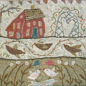 Op de afbeelding: Een vierkant kleed met een gehaakte textuur met een rood huis met een donker dak, een zwart boogvormig latwerk en drie vliegende bruine vogels. Het onderste gedeelte toont een beige veld met twee witte vogels tegenover elkaar tussen bloemen.