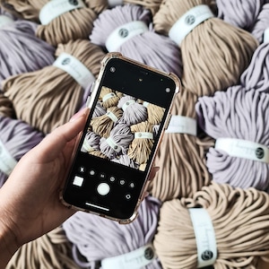 May include: A close-up of a smartphone camera screen displaying a variety of colorful yarn balls. The yarn is arranged in a circular pattern and is a mix of light and dark colors.