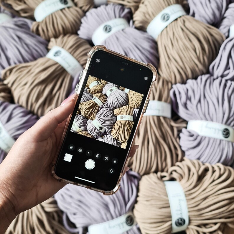 May include: A close-up of a smartphone camera screen displaying a variety of colorful yarn balls. The yarn is arranged in a circular pattern and is a mix of light and dark colors.