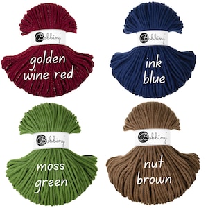 May include: Four bundles of Bobbiny macrame cord in golden wine red, ink blue, moss green, and nut brown. Each bundle is labeled with its color name. The cords are tightly wound, showcasing their texture and color variations, ideal for crafting projects.