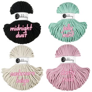 May include: Four spools of macrame cord in various colors: black with "midnight dust" text, mint green with "jelly mint" text, beige with "cashmere beige" text, and pink with "dusty rose" text. Each spool has a white label with the "Bobbing" logo.