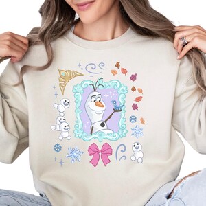 A woman wearing a beige sweater with a colorful graphic design featuring characters from the Disney movie Frozen.