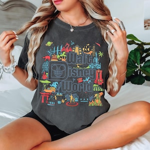 A woman wearing a gray t-shirt with a colorful graphic of Disney World landmarks and characters.