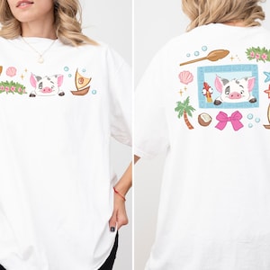 A woman wearing a white t-shirt with a colorful graphic design featuring a pig, palm tree, seashells, starfish, and other beach-themed elements.