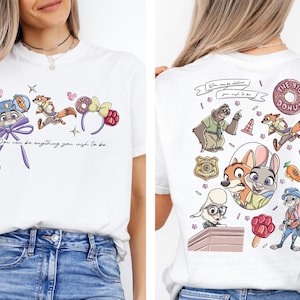 a white t-shirt with a colorful graphic design of cartoon characters, including a dog, a cat, and other animals, along with various objects like a donut and a carrot.
