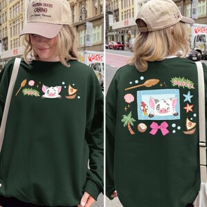 A woman wearing a green sweater with a pig design and various other decorative elements on the back.