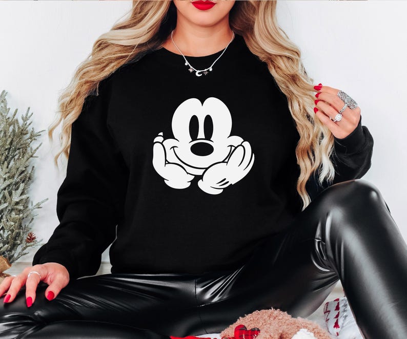 A woman wearing a black sweatshirt with a white Mickey Mouse logo is sitting on the floor.