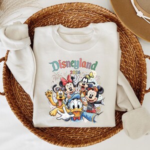 A white t-shirt with a colorful graphic of Disney characters from the theme park is displayed in a woven basket.