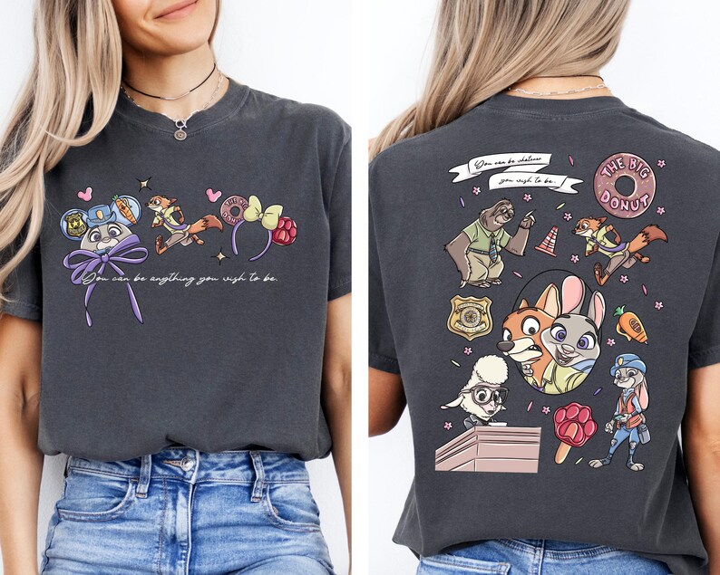 a woman wearing a gray t-shirt with a colorful graphic design on the back. The design includes cartoon characters such as a dog, a cat, and other animals, along with various objects like a donut, a hat, and a backpack. The text on the t-shirt reads "You can do anything you wish to be" and "The dog donut".