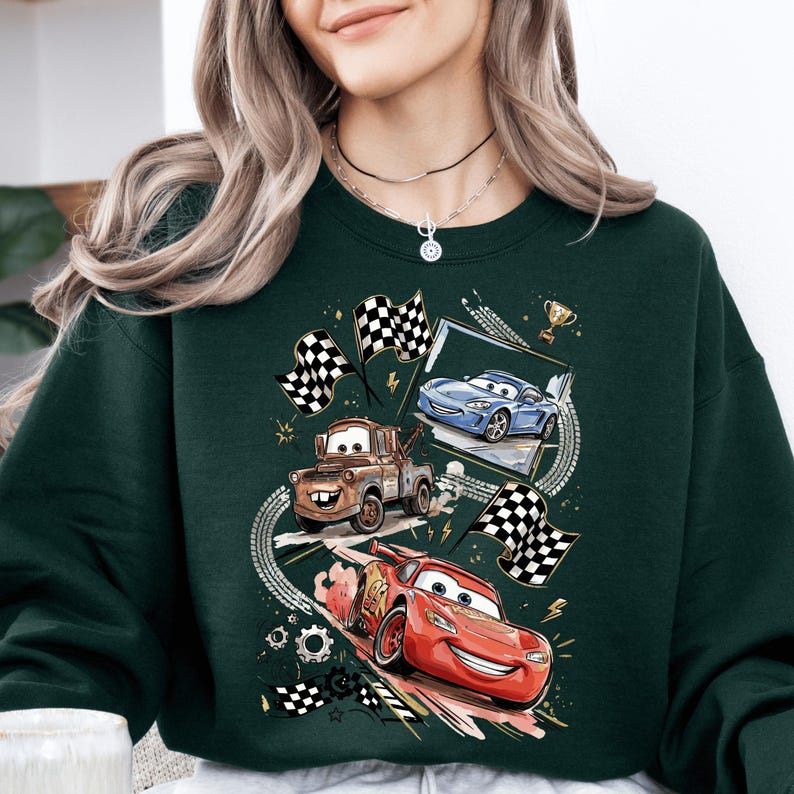 A woman wearing a green sweatshirt with a graphic design featuring three animated cars racing, including a red car, a blue car, and a brown truck.