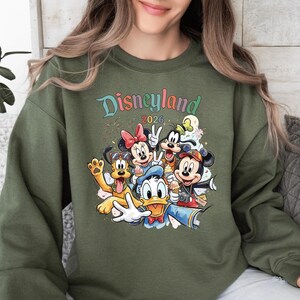 A woman wearing a green sweatshirt with a colorful graphic of Disney characters from the theme park.