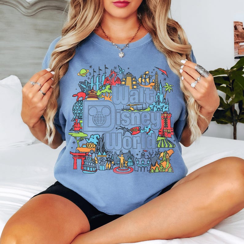 A woman wearing a blue t-shirt with a graphic design of various Disney landmarks and attractions.