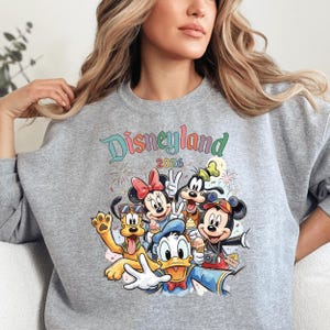 A woman wearing a gray sweatshirt with a colorful graphic of Disney characters from the theme park.