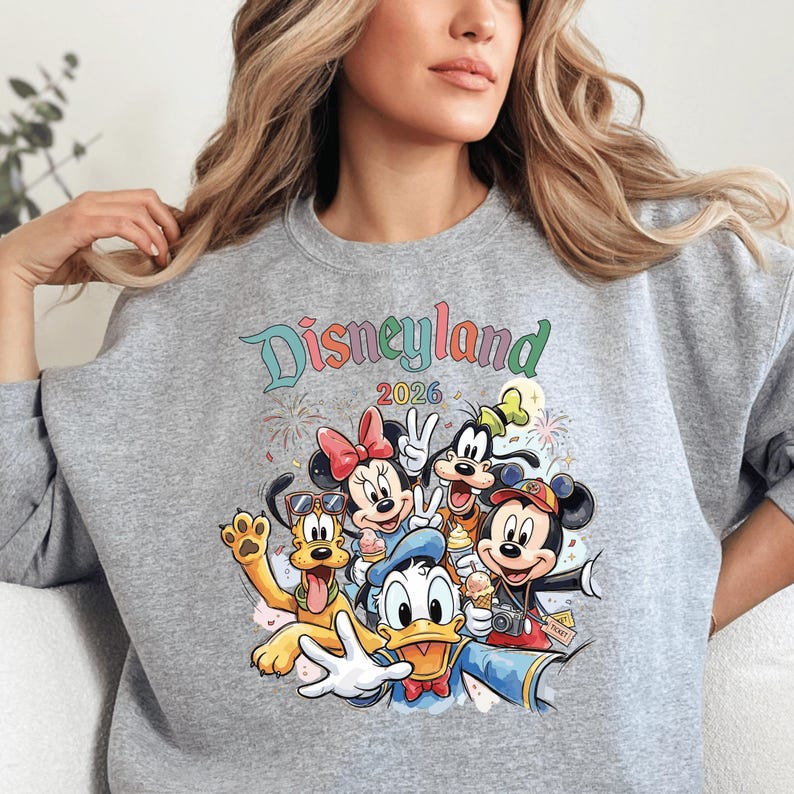 A woman wearing a gray sweatshirt with a colorful graphic of Disney characters from the theme park.