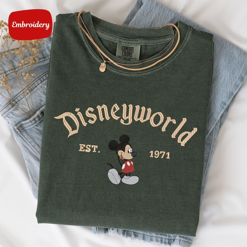 A green t-shirt with a Mickey Mouse design and text that says "Disneyworld EST. 1971" is displayed on a white surface.