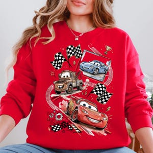 A red sweatshirt with a graphic design featuring cartoon cars and checkered flags, along with other racing-themed elements.