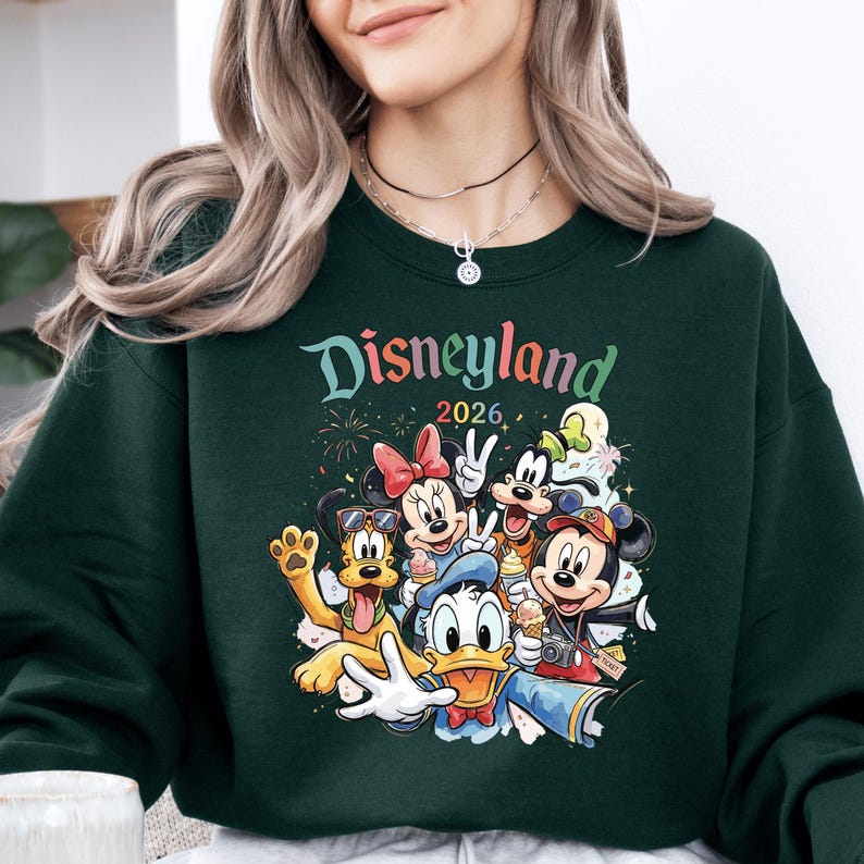 A woman wearing a green sweatshirt with a colorful graphic of Disney characters from the theme park.