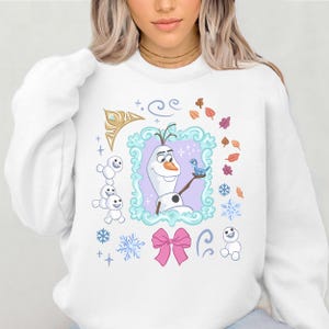 A woman wearing a white sweater with a graphic design featuring characters from the Disney movie Frozen.