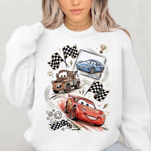 A white sweatshirt with a graphic design featuring characters from the animated movie Cars, including a tow truck, a blue car, and a red car.