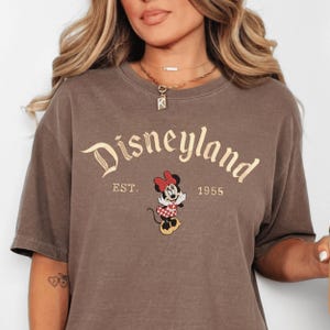 A woman wearing a brown t-shirt with the text "Disneyland EST. 1955" and an image of Minnie Mouse, a character from the Disney theme park.