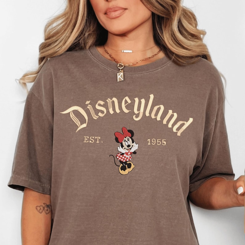 A woman wearing a brown t-shirt with the text "Disneyland EST. 1955" and an image of Minnie Mouse, a character from the Disney theme park.