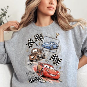 A woman wearing a grey sweatshirt with a graphic design featuring cartoon cars and racing flags.
