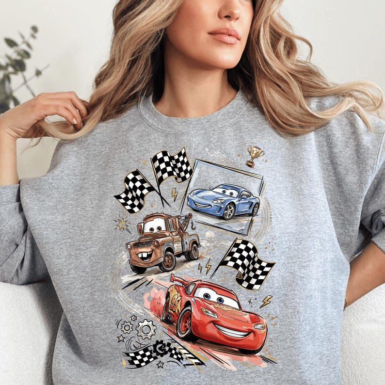 A woman wearing a grey sweatshirt with a graphic design featuring cartoon cars and racing flags.