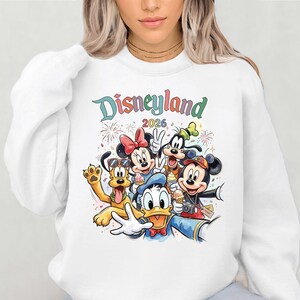 A woman wearing a white sweatshirt with a colorful graphic of Disney characters from the theme park.