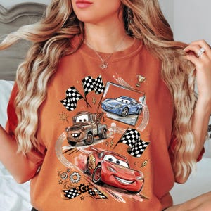 A woman wearing a t-shirt with a graphic design featuring animated cars from the Disney Pixar movie Cars.