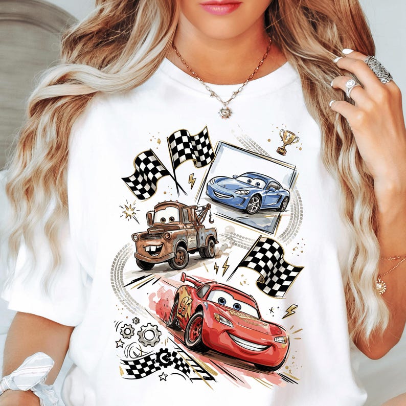 A white t-shirt with a graphic design featuring cartoon cars and racing elements, including checkered flags and lightning bolts.