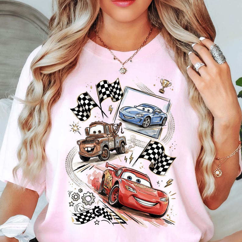 A woman wearing a pink t-shirt with a graphic design featuring cartoon cars and checkered flags.